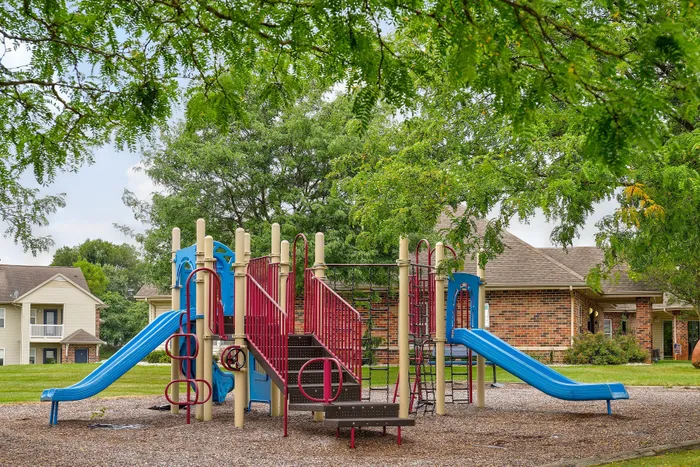 Charming community playground with vibrant slides and climbing structures, surrounded by lush greenery and attractive residential homes.