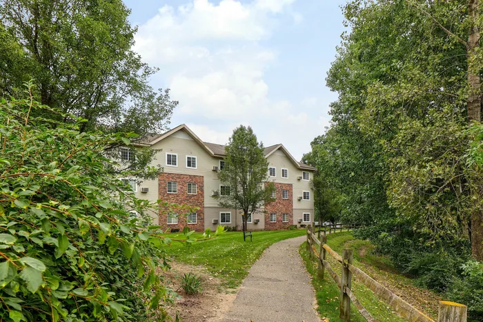 Charming apartment building nestled in lush greenery with a welcoming path and vibrant brick facade, perfect for nature lovers.
