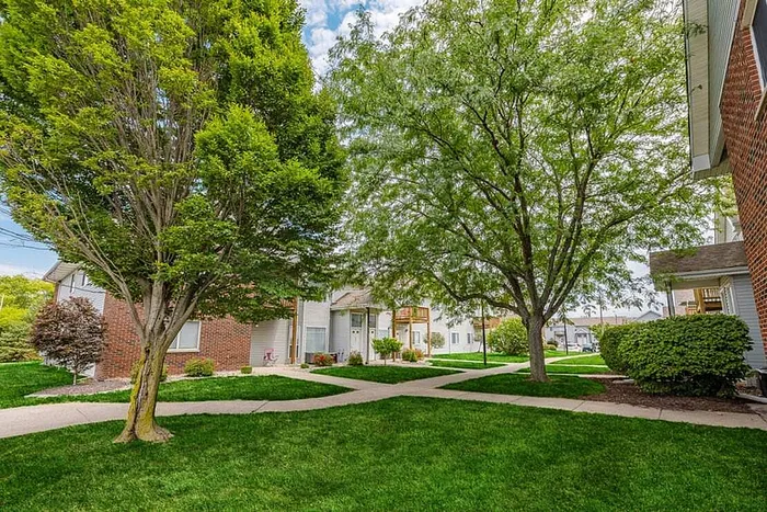 Charming apartment complex with lush green landscaping, mature trees, and inviting walkways, perfect for tranquil living.