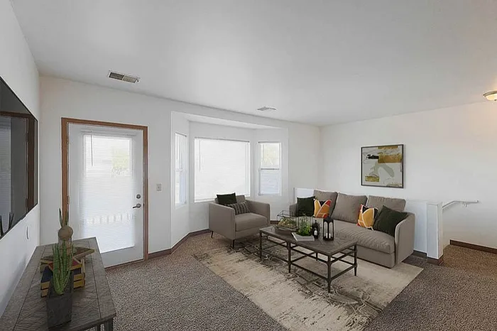 Bright and inviting living room with modern decor, featuring a comfortable sofa, stylish armchair, and contemporary art on the wall. Large windows allow natural light to illuminate the space, creating a cozy atmosphere.