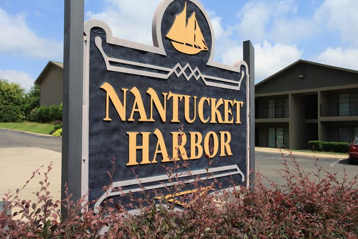Charming Nantucket Harbor sign with nautical motif, set against a backdrop of lush greenery and modern apartments.