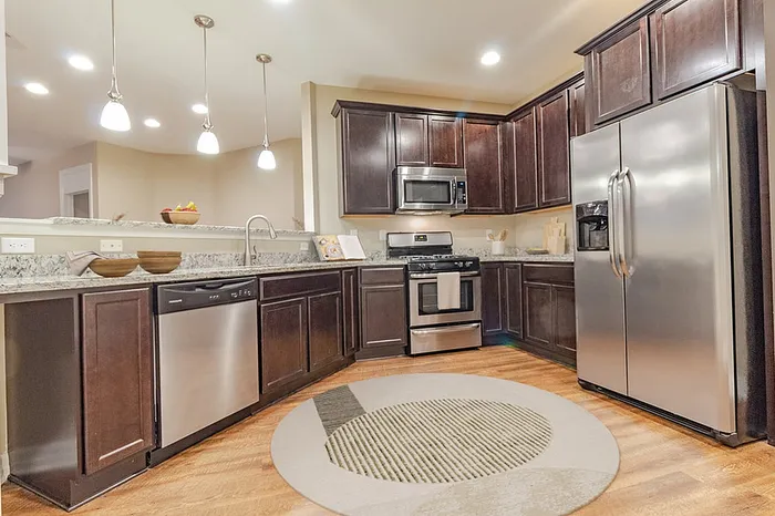 Modern kitchen with elegant dark wood cabinets, stainless steel appliances, and stylish pendant lighting over a granite countertop.