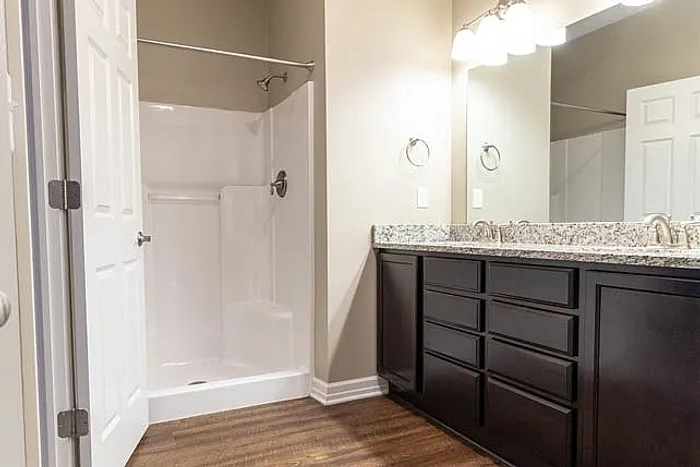 Elegant bathroom with dark wood cabinetry, large mirror, granite countertops, and a spacious walk-in shower.
