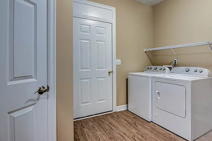 Modern laundry room with sleek washer and dryer units, featuring elegant laminate flooring and ample shelving.