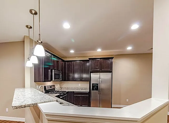 Chic kitchen with elegant dark wood cabinetry, modern stainless steel appliances, and sleek granite countertops illuminated by stylish pendant lights.