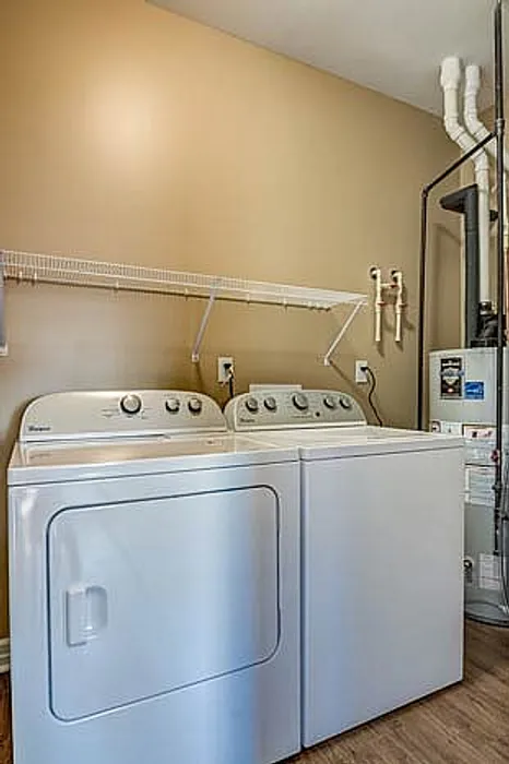 Modern laundry room featuring a high-efficiency washer and dryer set against a warm beige wall, complete with convenient open shelving and sleek utility access.