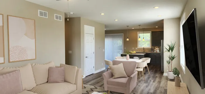 Modern living room with elegant beige sofa, chic pink armchair, and contemporary dining area leading to a stylish kitchen with dark cabinetry.