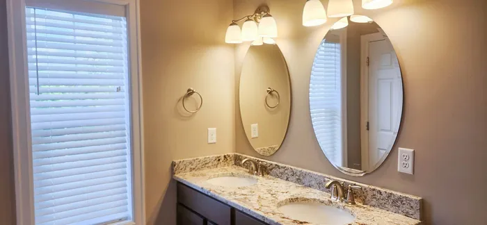 Elegant bathroom with dual sinks, granite countertop, and ambient lighting, complemented by a large mirrored wall and window with modern blinds.