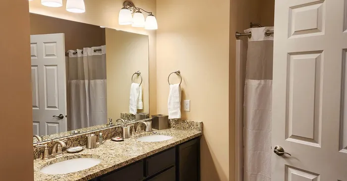 Elegant bathroom featuring dual sinks with granite countertop, stylish lighting, and a modern shower area.