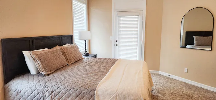 Cozy bedroom featuring a plush king-sized bed, modern lamp, and elegant wall mirror creating a warm, inviting atmosphere.