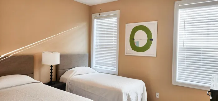 Bright and cozy bedroom with twin beds, modern art, and ample natural light filtering through blinds.
