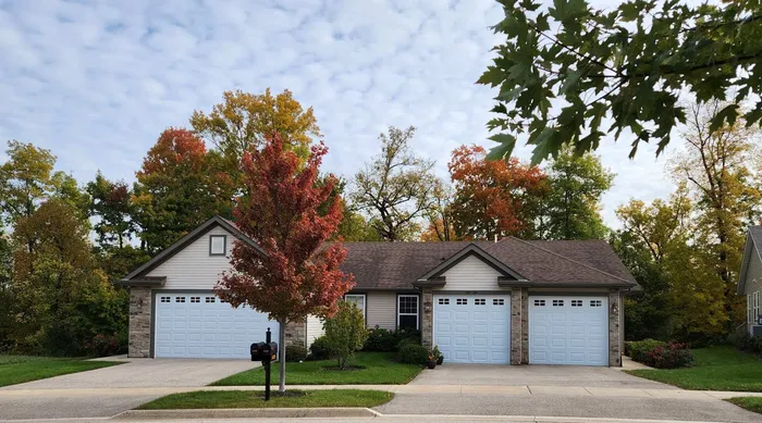Charming duplex with double garages nestled in a serene neighborhood surrounded by vibrant autumn trees.