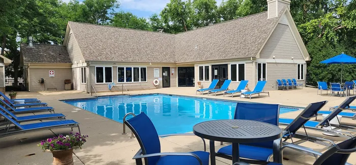 Spacious outdoor pool area with modern loungers, vibrant blue seating, and lush greenery, perfect for relaxation and leisure.