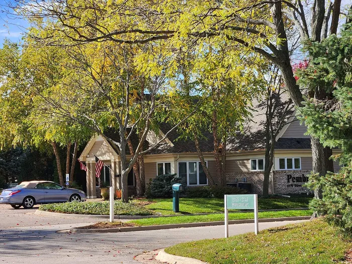 Charming residential building surrounded by lush greenery and vibrant autumn foliage, featuring a welcoming entrance and a parked convertible.