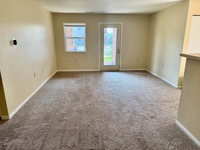 Bright and inviting living area with plush carpeting, a large window, and a glass door leading to outdoor space, ideal for a cozy home atmosphere.