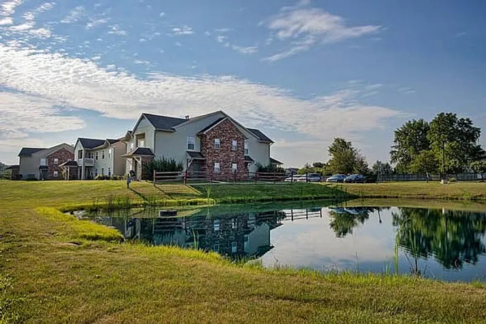 Charming two-story apartment buildings with a beautiful pond reflection under a bright, clear sky, showcasing serene and picturesque living.