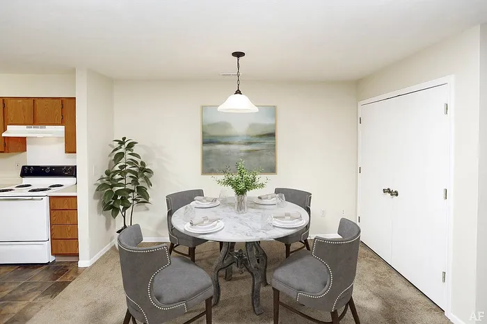 Inviting dining area with modern round marble table, stylish gray chairs, and ambient lighting next to a cozy, functional kitchen.