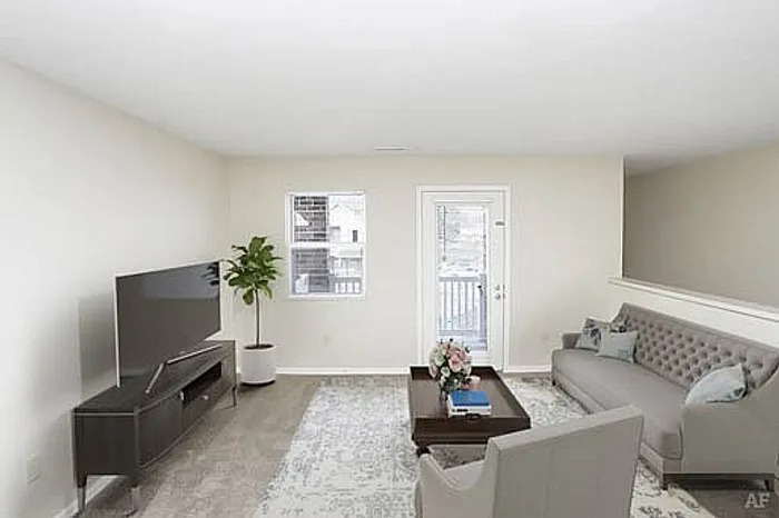 Bright living room with elegant decor, featuring a large TV, cozy seating area, and access to a balcony.