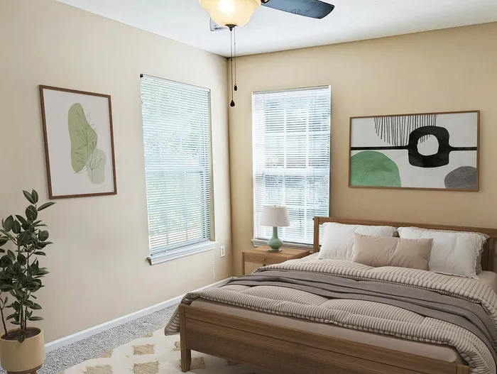 Bright and cozy bedroom with modern decor, featuring stylish artwork, a plush bed with layered bedding, and sunlit windows framed by light blinds.