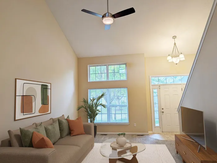 Bright living room with tall ceilings, comfy sofa with colorful pillows, contemporary art, and modern lighting. Sunlit windows enhance the inviting ambiance.