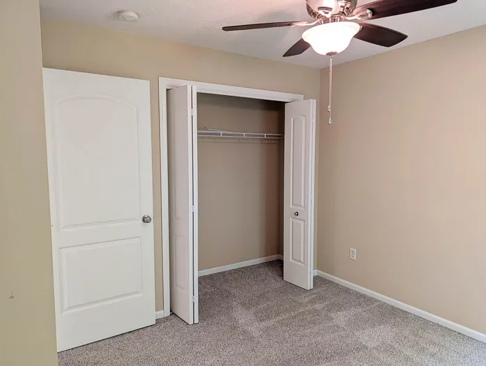 Inviting bedroom with plush carpet, neutral walls, spacious closet, and elegant ceiling fan.