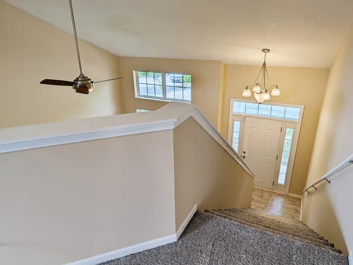 Inviting staircase with a modern overhead fan, plush carpeted steps, and elegant light fixture, leading to a bright entrance hall with ample windows.