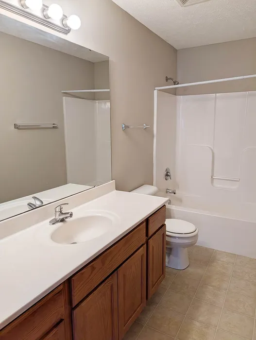 Modern bathroom with elegant vanity, spacious mirror, and a clean white tub surrounded by neutral walls, perfect for relaxation.