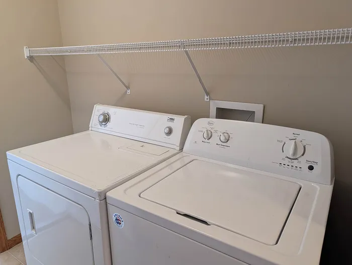 Modern laundry room featuring sleek white washer and dryer set with convenient wall-mounted shelving.