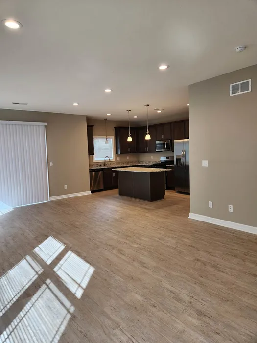Inviting open-concept kitchen and living area with elegant lighting, premium hardwood floors, and modern dark cabinetry.