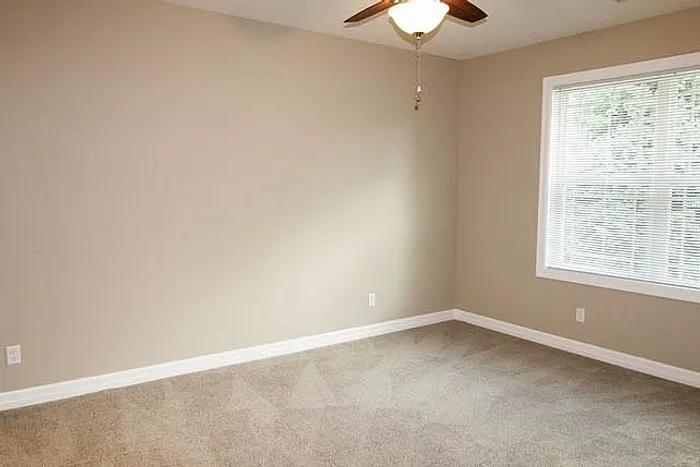 Bright and spacious bedroom with neutral walls, large window, and ceiling fan, offering comfort and style.