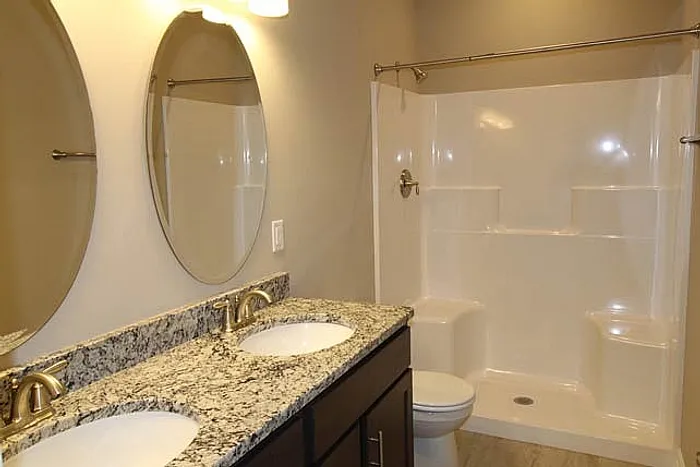 Modern bathroom with elegant granite countertop, dual sinks, and a sleek shower enclosure.