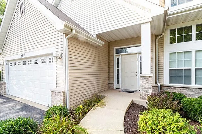 Charming entryway of a modern home featuring a welcoming front door, lush landscaping, and attached garage, offering curb appeal and convenience.