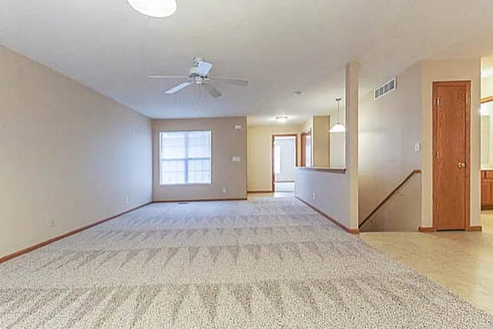 Spacious, well-lit living area with plush carpeting and modern ceiling fan, perfect for family gatherings.