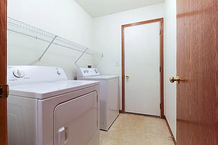 Bright laundry room with modern washer and dryer, featuring ample shelving for storage and a sleek tiled floor.