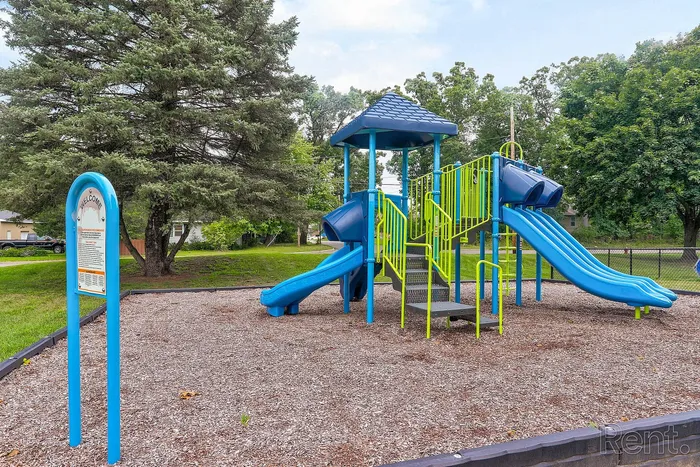 Inviting playground featuring bright blue slides and a vibrant climbing structure, surrounded by lush green trees in a welcoming outdoor setting.