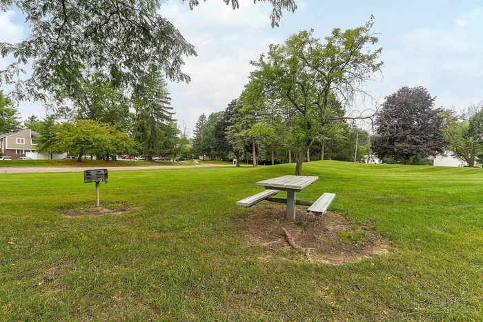 Inviting park setting with a picnic table, surrounded by lush greenery and mature trees, ideal for outdoor relaxation.
