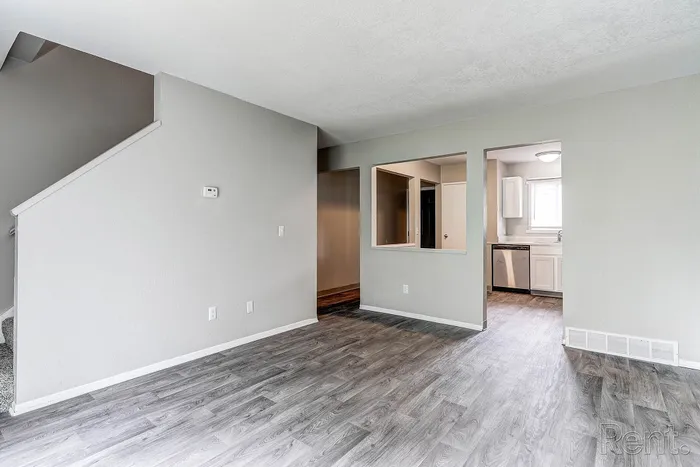 Bright and spacious living area featuring sleek laminate flooring, open staircase, and a modern kitchen entrance.