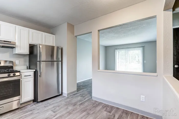 Bright kitchen with sleek stainless steel appliances and open window to a sunlit living room, featuring elegant flooring and modern cabinetry.
