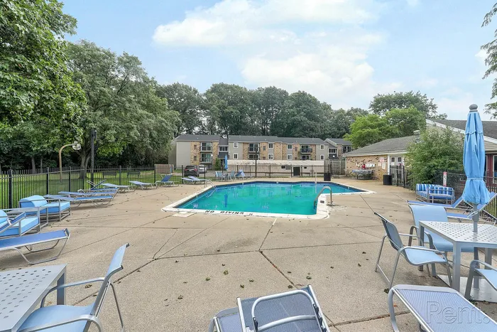Inviting outdoor pool area with modern lounge chairs and umbrellas, surrounded by lush greenery and apartment buildings, offering a relaxing retreat.
