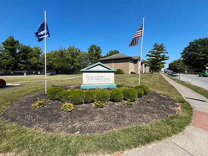 Charming entrance to Meadows at Greentree, highlighted by vibrant landscaping and flags, creating a welcoming atmosphere.