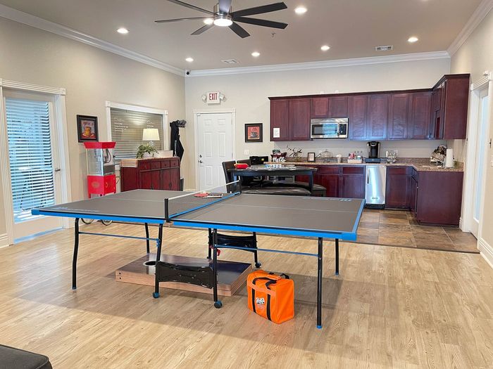 Contemporary recreation room featuring a sleek ping pong table, elegant kitchenette with rich wooden cabinetry, and stylish decor for a perfect entertainment space.