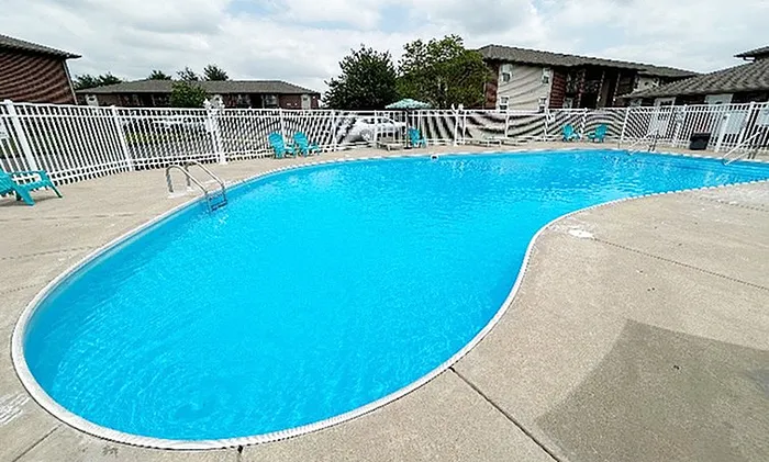 Inviting kidney-shaped outdoor pool surrounded by a spacious patio and white fencing, perfect for relaxation and enjoyment.