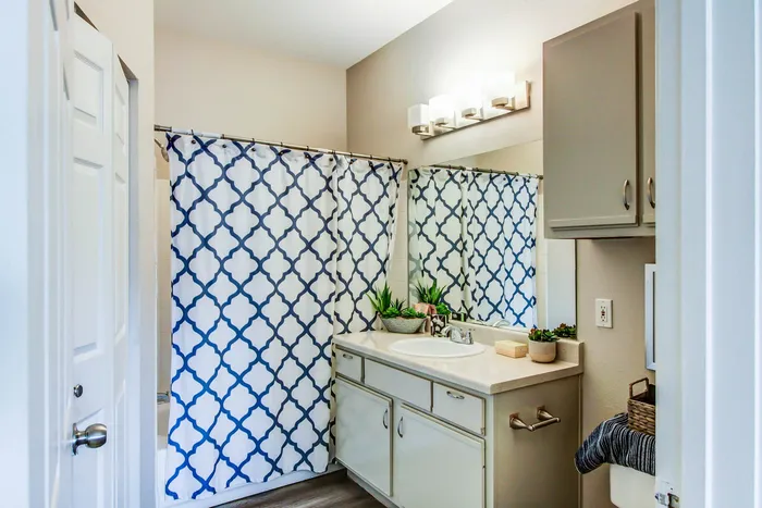 Chic bathroom featuring a modern vanity, elegant lighting, and stylish patterned shower curtain with lush green plants for a serene ambiance.