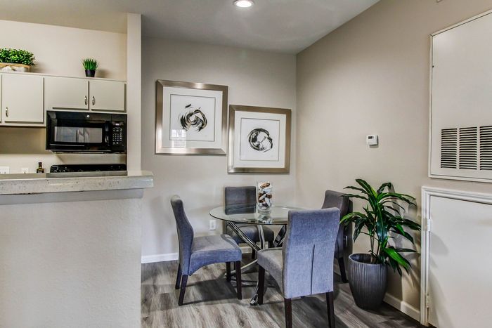 Inviting dining area with a modern glass table, elegant gray chairs, and stylish wall art near a cozy kitchen with sleek cabinetry.