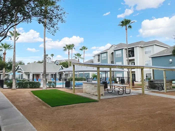 Beautiful apartment complex with a refreshing pool, lush green landscaping, and charming pergola picnic area under a sunny sky.