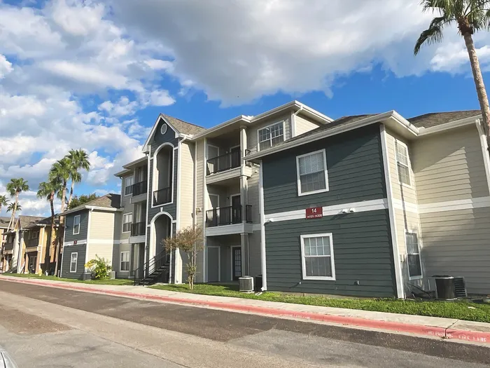 Charming multi-story apartment complex with elegant architectural details, surrounded by lush palm trees and a vibrant blue sky backdrop.