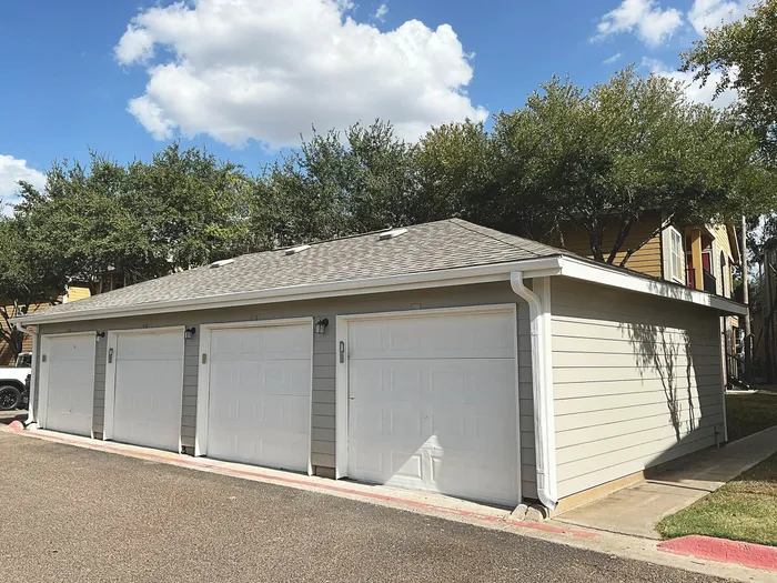 Modern apartment complex with spacious private garages, surrounded by lush trees and a clear blue sky.