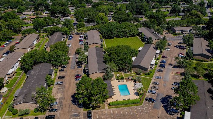 Charming aerial view of a spacious apartment complex surrounded by lush greenery, featuring a welcoming swimming pool and ample parking.