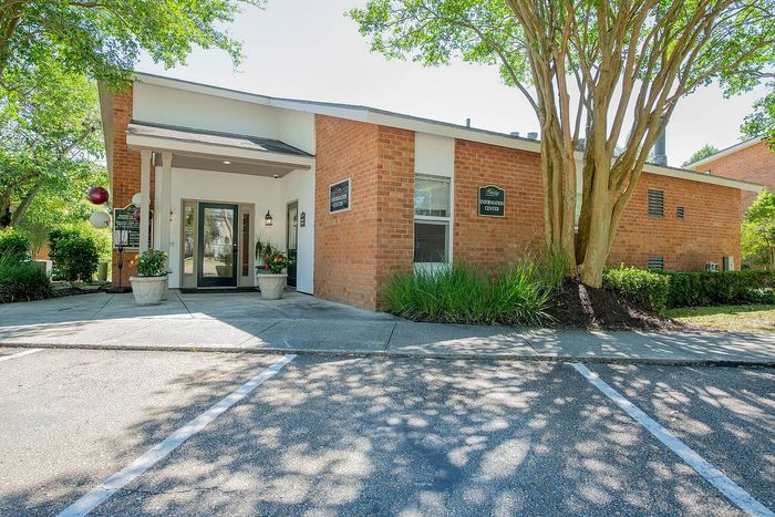 Charming apartment complex entrance featuring brick facade, lush greenery, and welcoming information center with modern design.