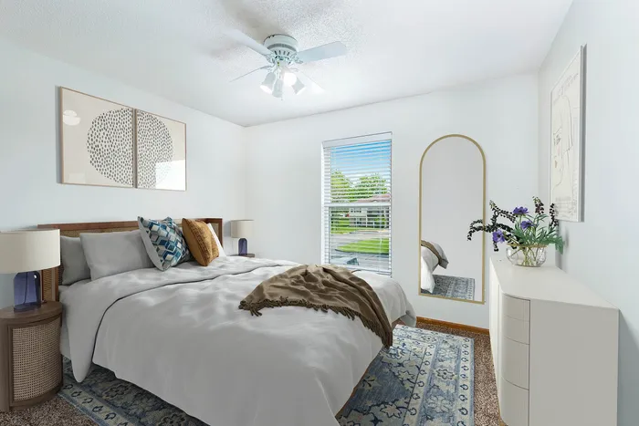 Bright and cozy bedroom featuring a stylish bed with decorative cushions, large window with blinds, elegant mirror, and tasteful artwork. Perfect blend of comfort and design.